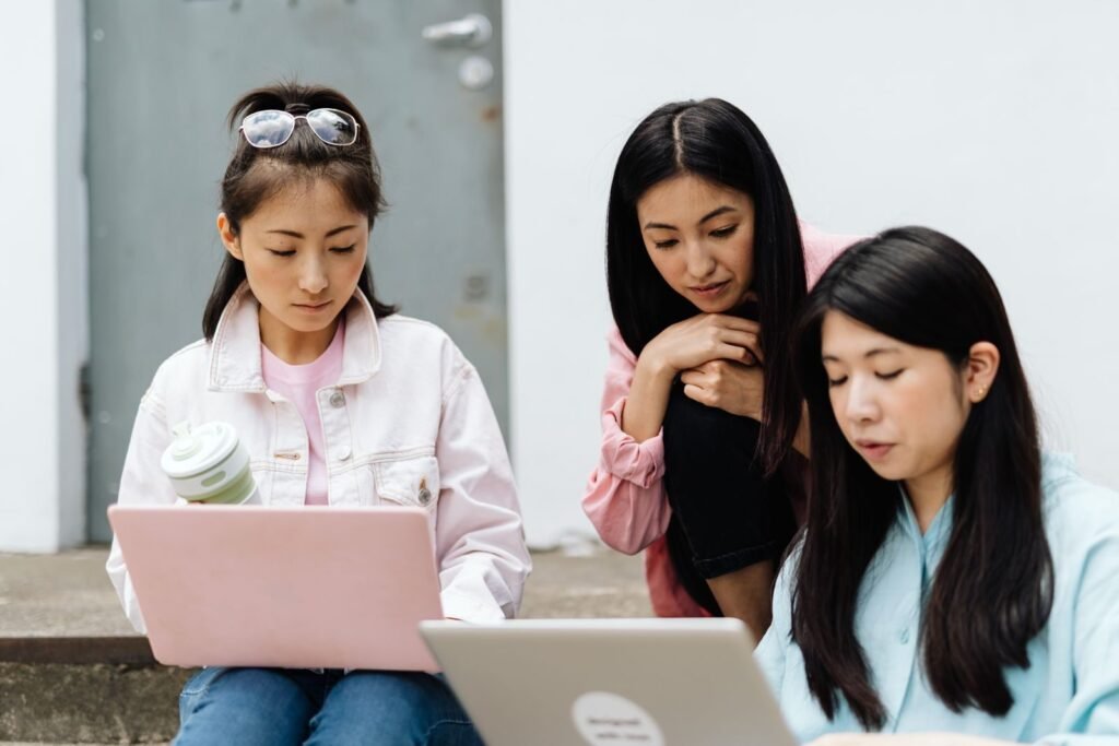 Three young women working together on laptops outdoors, representing retaking the Rice Purity Test