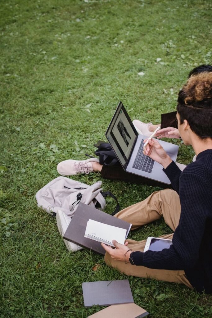 Two students studying together on a laptop outdoors surrounded by books, tracking Rice Purity Test scores over time